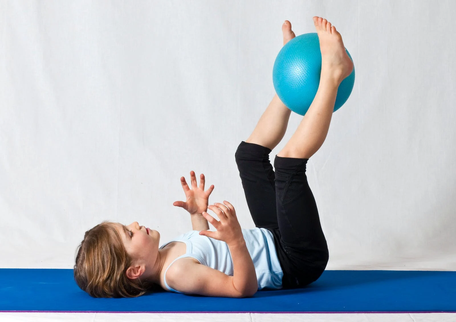 Young girl lying on her back with ball up in the air between her feet.